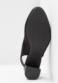 Chaussure ouverte à l'arrière en suède noir, vue en angle vers le haut, montrant la semelle lisse et le talon bas carrée texturé sur fond blanc.