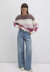 Chunky knit sweater with wide horizontal stripes in mauve, pink, and cream. Paired with loose-fit light blue jeans and beige shoes.