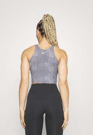 Vrouw met lang gevlochten haar die een zwart-wit patroon crop top en hoge taille zwarte legging draagt, staand met haar rug naar de camera.
