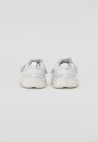 Witte sportieve schoenen met een gestructureerde mesh bovenkant, gevoerde kraag en klittenbandsluiting. Afgeronde zool met een minimaal loopvlakpatroon. Achteraanzicht.