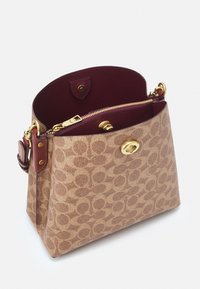 Tan patterned handbag with a structured shape. Features a burgundy interior, gold hardware, zip closure, and a detachable strap.