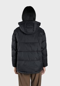 Veste matelassée noire avec capuche, design en losanges et poignets élastiques. Présente un matériau lisse et une coupe mi-longue. Vue arrière montrée.