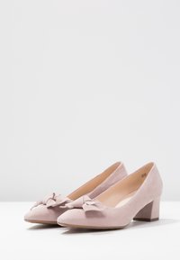 Chaussures à talons blocs en suédine rose avec un bout arrondi et un nœud décoratif à l'avant. Texture lisse avec une finition légèrement mate.