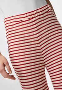 Pantalons en tricot rayés rouge et crème avec une taille élastique. Le tissu semble doux et texturé, présentant des rayures horizontales uniformes.