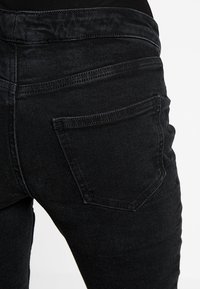 Jeans de mezclilla negra con un diseño ajustado, que presentan un bolsillo trasero estándar y una textura suave, mostrados de lado.