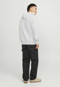 Grijze sweater met een capuchon, gecombineerd met zwarte cargobroeken met witte stiksels en zakken. Schoenen zijn beige suède pantoffels.