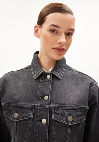 Donkergrijze denimjas met een kraag, voorzien van zilveren drukknoopsluitingen en twee borstzakken met kleppen, gemaakt van een gestructureerde stof.