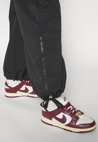 Svarta baggybyxor med dragkedjefickor, i kombination med röda och vita Nike-sneakers. Sneakers har strukturerat material och en 'Just Do It'-logotyp.