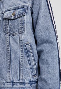Jasnoniebieska kurtka dżinsowa o postarzanym wyglądzie, z kieszeniami z przodu, zapięciem na guziki oraz paskowanymi akcentami na rękawach.