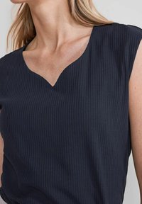 Námořnický pruhovaný top s výstřihem do V a krátkými rukávy, vyrobený z texturované látky. Design je jednoduchý a přiléhavý.