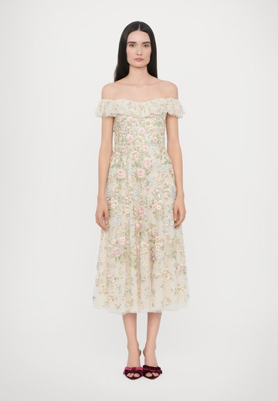 Off-shoulder bloemengeborduurd jurk in zacht beige met pastelrozen, gelaagd tule en een vloeiende silhouet. Fluwelen schoenen maken de look compleet.