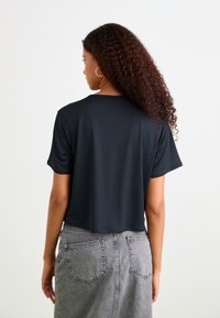 Zwart cropped t-shirt van gladde stof, met korte mouwen en een ronde halslijn, gecombineerd met een grijze denim rok met achterzakken.