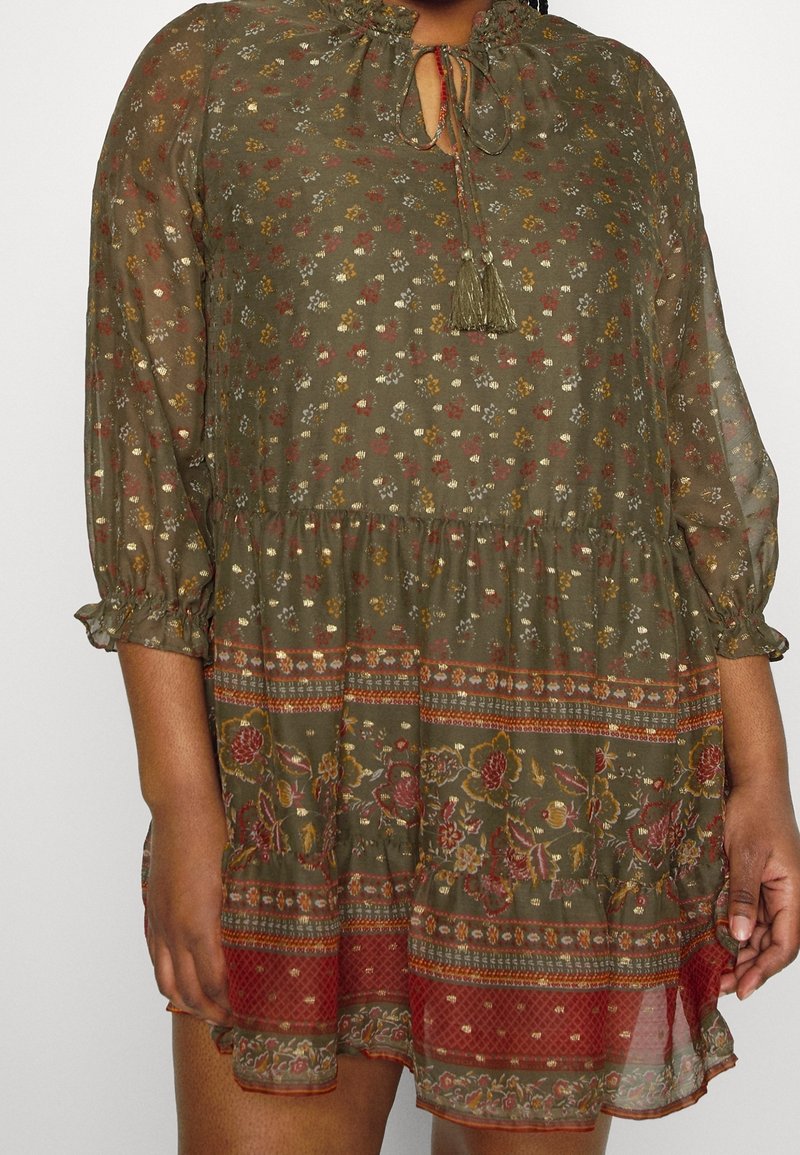 Donkergroene jurk met bloemenprint, geplooide hals, en strikdetail. Vloeiende stof, driekwartmouwen, en een tiered zoom met bloemenaccenten.