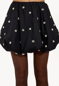 Jupe noire froncée ornée d'embellissements en forme de fleurs blanches, taille élastique et silhouette bouffante. Texture de tissu lisse.