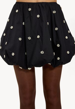 Schwarzer geraffter Rock mit weißen, blumenförmigen Verzierungen, elastischem Bund und einer voluminösen Silhouette. Glatte Stoffstruktur.