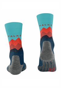 Un paio di calzini multicolore con talloni e punte grigie, design di montagne blu e rosse, e testo "FALKE" sui polsini azzurri.