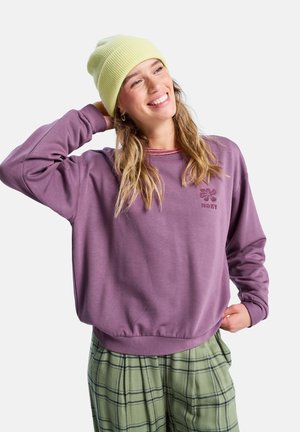 Pullover sweatshirt in zacht paars met een ronde hals en ribgebreide mouwen. Voorzien van een bloemenlogo in een donkerder paars. Gepaard met groene plaid broeken.