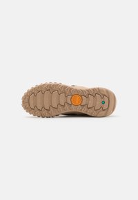 Rubberen zool met diepe grippatronen, voornamelijk beige met een oranje cirkelvormig logo. Ontworpen voor duurzaamheid en grip op verschillende oppervlakken.