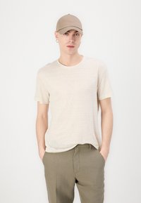 Beige bomulls t-skjorte med rund hals og korte ermer, kombinert med olivengrønne linbukser og en matchende beige caps.