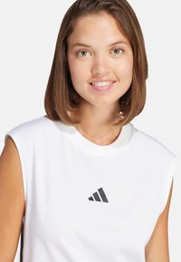 Camiseta sin mangas blanca de algodón, con un logo negro de Adidas en el frente, escote redondo y textura suave.