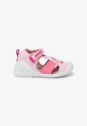 Scarpa in tessuto rosa con punta chiusa e design a ritagli, cinturino in velcro regolabile, suola in gomma bianca e accenti ricamati colorati.