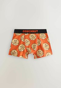 Caleçons boxeurs orange avec une ceinture noire portant l'inscription « DOUGHNUT », imprimés de donuts dessinés en style cartoon avec des visages souriants répétitifs.