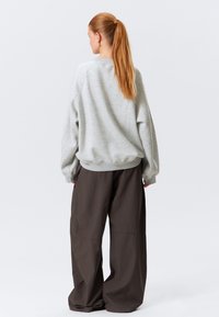 Sudadera gris de corte relajado, con puños acanalados y escote redondo, combinada con pantalones holgados de color marrón oscuro, ambos en una tela suave.