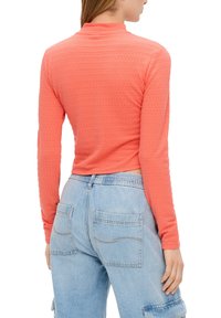 Garais jāņos ar garām piedurknēm, izgatavots no teksturēta auduma. Iespējamais augstais apkakle un īsā piegriezuma, saskaņots ar gaiši ziliem, plašiem džinsiem ar kabatām.