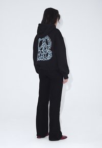 Felpa nera con un design floreale blu sul retro, polsini a coste e una vestibilità rilassata, abbinata a pantaloni neri svasati e scarpe rosse.