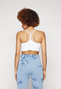 Soutien-gorge de sport blanc avec des bretelles croisées dans le dos, associé à un legging bleu clair avec un motif marbré et une texture lisse.