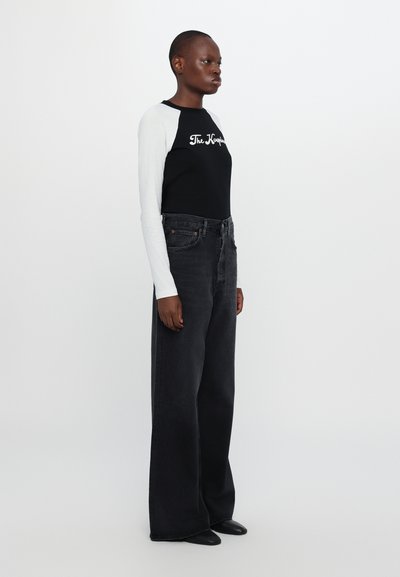 Black and white long-sleeve shirt with text logo, paired with high-waisted black wide-leg jeans. Smooth fabric with casual fit.
