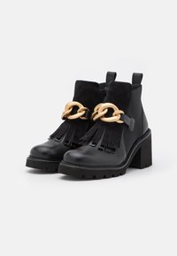 Černé kotníkové boty vyrobené z kůže a semiše, s předními třásněmi, zlatým řetízkovým detailem a masivním podpatkem. Robustní podrážka pro lepší trakci.