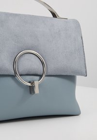 Sac à main en cuir et daim bleu clair avec fermoir anneau métallique argenté et poignée, photographié sur un fond clair uni.