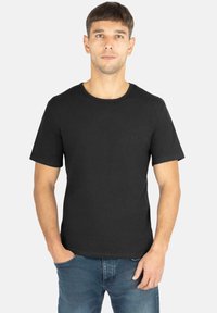 Schwarzes T-Shirt mit kurzen Ärmeln und rundem Halsausschnitt, aus weicher Baumwolle, mit einem dezenten Logodetail auf der Brust. Kombiniert mit blauen Jeans.