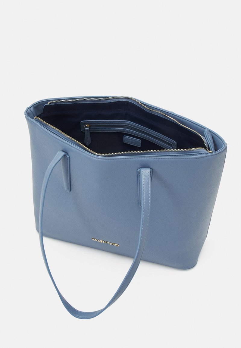 Blauwe tote bag gemaakt van textuurmateriaal. Beschikt over twee handvatten, ritsluiting en gouden branding aan de voorkant. Rectangulaire vorm met interne compartimenten.