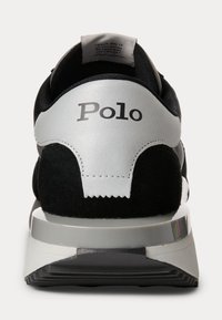 Černé tenisky se stříbrnou patou, s jemným svrchním materiálem, kontrastními texturami a tištěným logem. Podešev má vícestupňový design.