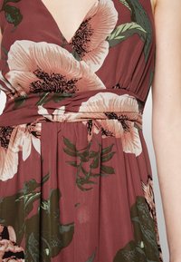 Blommig klänning i dämpad bordeaux med stora rosa blommor och gröna blad. Har en omslagsdesign och plisserad kjol, tillverkad av lättviktig tyg.