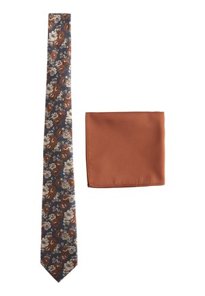 Schmale Krawatte mit blauem, braunem und weißem Blumenmuster neben einem einfarbigen Einstecktuch in Rostfarbe auf weißem Hintergrund.
