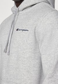 Szary hoodie wykonany z miękkiej, teksturowanej tkaniny. Posiada przednią kieszeń, regulowany kaptur ze sznurkiem oraz haftowane logo "Champion".