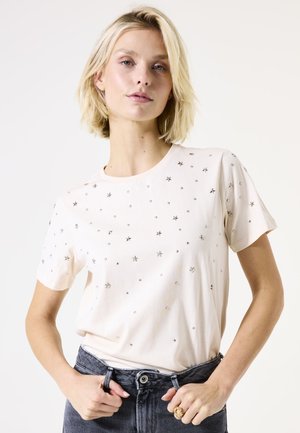 T-shirt rose clair à manches courtes avec des embellissements en étoiles et en gemmes argentées dispersées, encolure ronde et coupe décontractée. Porté avec un jean foncé.