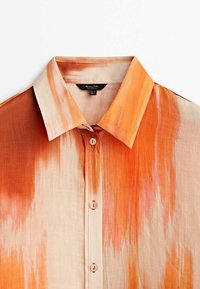 Chemise à manches courtes en tissu léger, présentant un motif aquarelle orange et rose, un col pointu et une fermeture à boutons sur le devant.