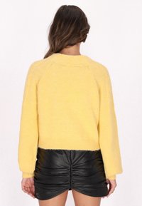 Pulover galben pufoș cu un design scurt și mâneci lungi, asociat cu o fustă neagră din piele ecologică plisată.