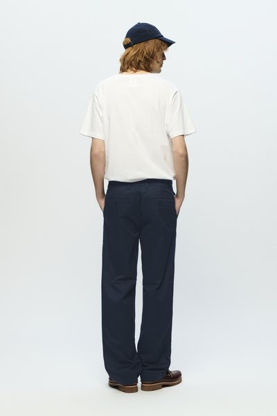 T-shirt en coton blanc, pantalons bleu marine et casquette bleu marine. Coupe ample, design simple, et détails de texture du tissu non visibles. Les chaussures ont des accents marron.