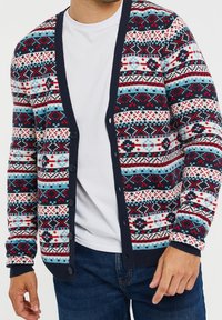 Knitted cardigan in multicolor patterns of red, blue, and white. Features a navy blue trim and front buttons, made of soft material.