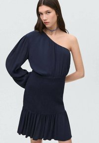 Mornarsko enooko obleko z strukturiranim, tekočim vrhom in prilegajočo teksturirano krilo, ki vključuje nabrano obrobje in dolgo balonsko rokav.