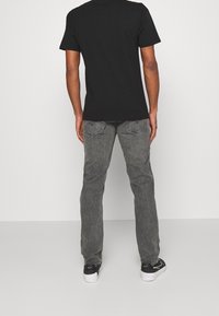 Camiseta negra de manga corta combinada con jeans de denim gris que presentan una textura sutil y costuras en contraste; llevada con zapatillas negras y blancas.