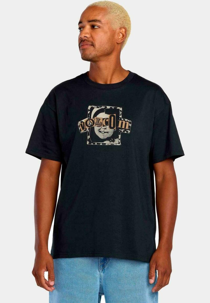 Camiseta de algodón negra con cuello redondo, que presenta un diseño gráfico en beige y gris, que representa una cara y el nombre de la marca "VOLCOM" en el centro.