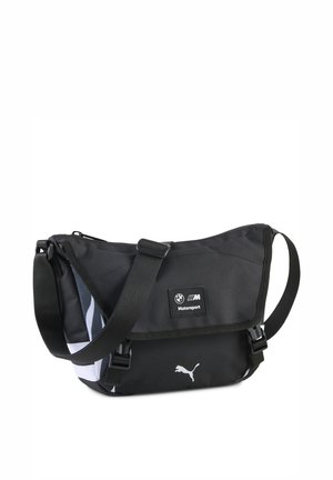 Sort crossbody taske fremstillet af slidstærkt stof, med klaplukning, justerbar rem og logo-detaljer i hvid og grå.