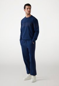 Donkerblauwe sweatshirt met textuurpanelen en bijpassende broek, met een relaxte pasvorm en een elastische tailleband, gecombineerd met witte sneakers.