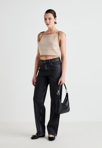 Strikket cropped top med striber i beige og creme, højtaljede sorte denimbukser, sorte flade sko og en sort håndtaske med sølvhardware.
